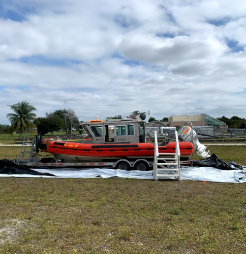 A boat with an inflatable orange base surrounded by a tarp in the middle of a field.