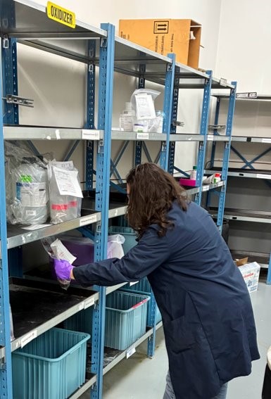 woman places a packaged bottle on a shelf organized with other containers in plastic bags.
