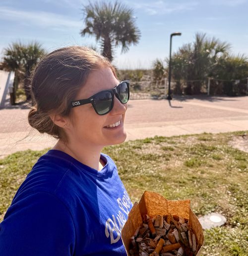 Woman holds brown paper bag filled with cigarette butts.