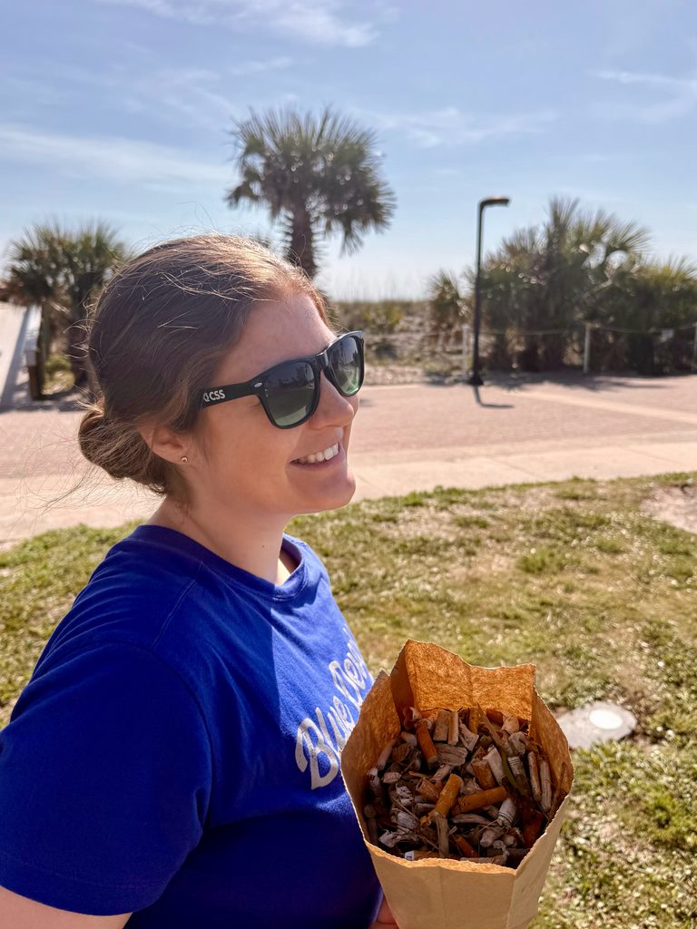 Woman holds brown paper bag filled with cigarette butts.